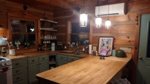 Une cuisine chaleureuse avec des meubles en bois, un îlot central, des luminaires suspendus et un appareil de climatisation.