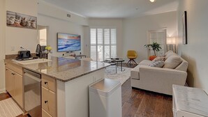 Una cocina moderna con una isla grande, un comedor con una silla amarilla y una sala de estar con un sofá color beige.
