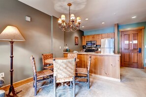 A modern kitchen with a round dining table, wicker chairs, a chandelier, wooden cabinets, and a refrigerator. - 1 Bedroom Condo (Keystone)