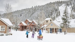 Un village enneigé avec des bâtiments en bois et une piste de ski en arrière-plan.
