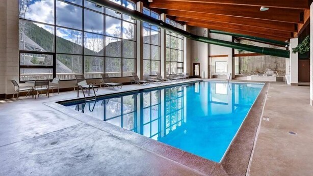 Une piscine intérieure dotée de grandes baies vitrées, de poutres en bois au plafond et de chaises longues.