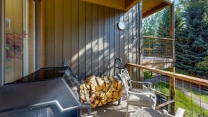 Un balcon avec un barbecue, une pile de bois de chauffage et une chaise.