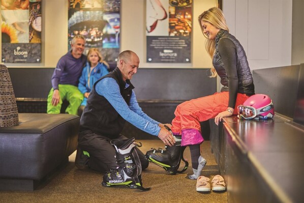 A person adjusting a helmet on a bench in a public area with seating and posters on the walls. - 2 Bedroom Residence (Vail)