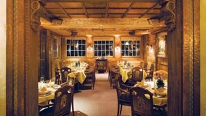 Zona pranzo con diversi tavoli e sedie, soffitto in legno e ampie finestre.