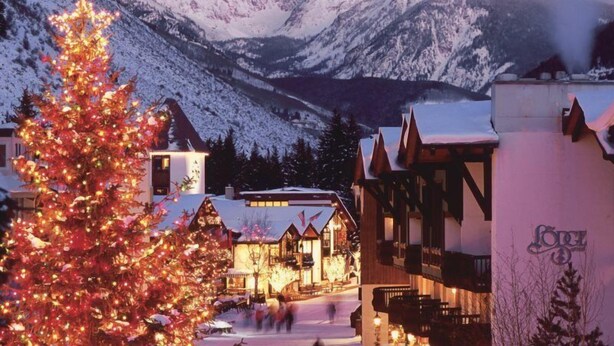 Un paese montano innevato con edifici in legno tradizionali e un abete di Natale ben visibile.