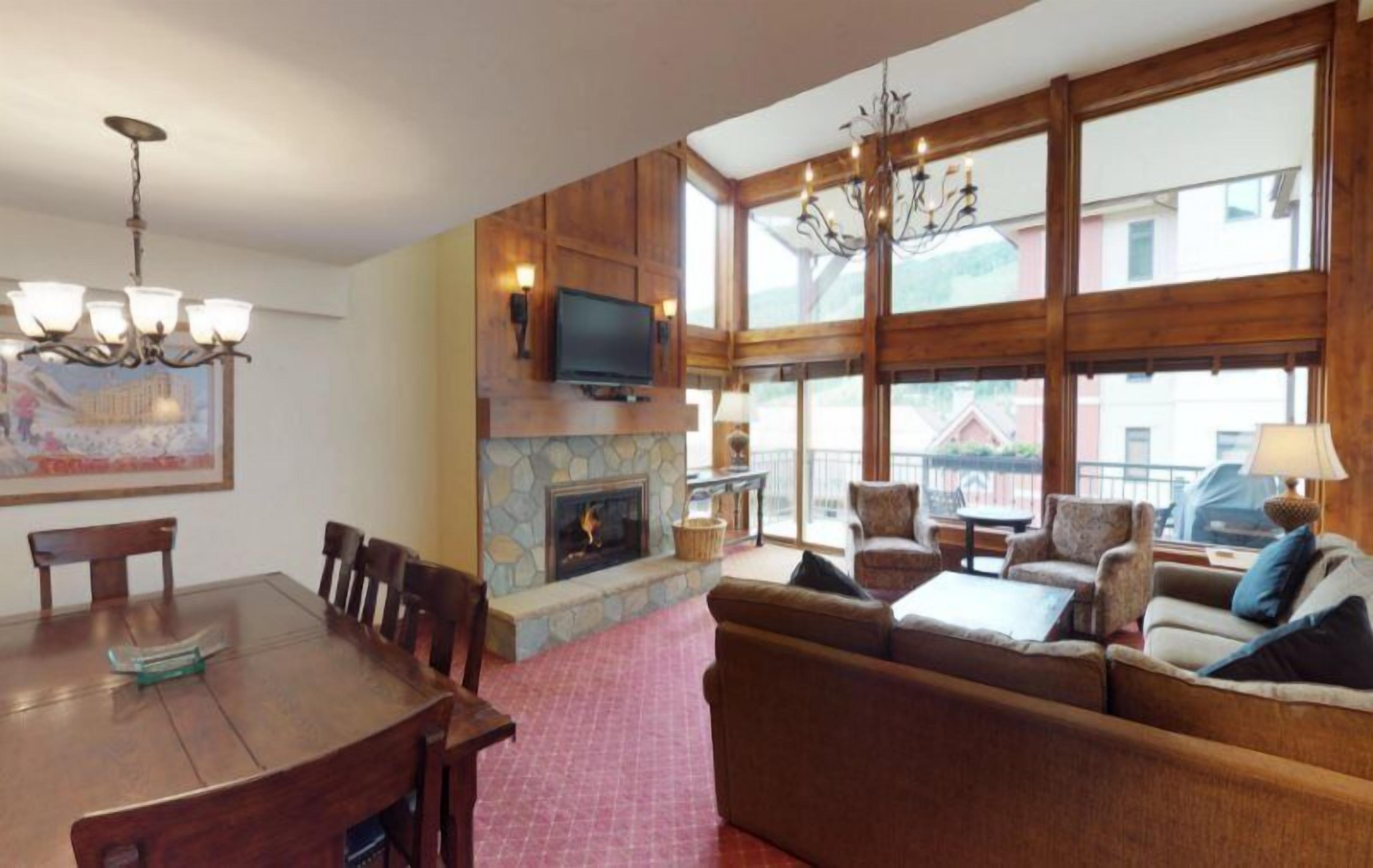 A spacious living room with a fireplace, a dining area, and large windows offering a view of the outside.