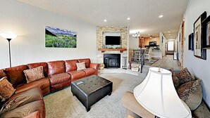A living room with a brown leather sofa, a black ottoman, a white lamp, and a fireplace. - 3 Bedroom Condo (Keystone)