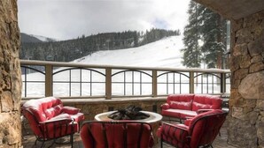 A stone-floored balcony with red leather chairs and a central fire pit, overlooking a snowy mountain slope. - 1 Bedroom Condo (Keystone)