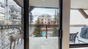 A balcony with a metal railing, a bench, and a view of a building with a red facade and a tree in the background. - 2 Bedroom Condo (Vail)