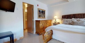 A bedroom with a bed, wooden dresser, nightstand, lamp, and a television on the wall. - 1 Bedroom (Vail)
