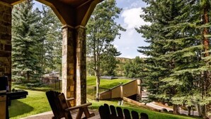 A covered patio with Adirondack chairs, a grill, and a view of a forested area. - 3 Bedroom Residence (Snowmass Village)