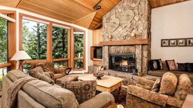 A cozy living room with a stone fireplace, large windows, and wooden ceiling. - 3 Bedroom Residence (Snowmass Village)