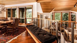 A spacious room with a wooden ceiling, large windows, a dining area, and a seating area with a black cushioned bench. - 3 Bedroom Residence (Snowmass Village)