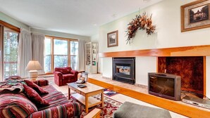 A cozy living room with a fireplace, a sofa set, a coffee table, and a television. - 1 Bedroom Condo (Keystone)