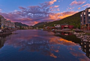 A riverside town with buildings along the water, a mountain backdrop, and a clear sky. - 1 Bedroom Condo (Keystone)