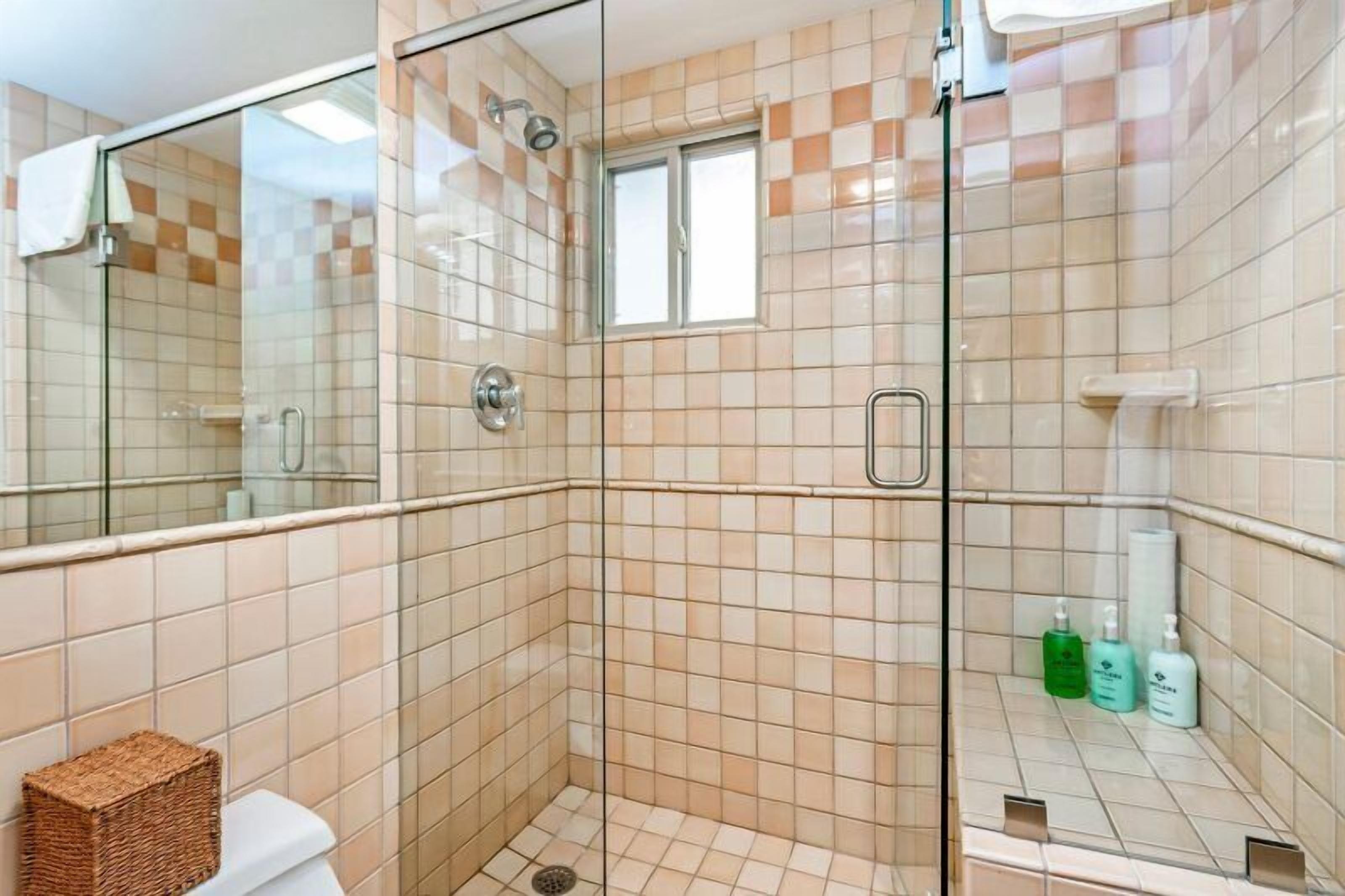 Une salle de bain avec une douche à parois de verre, une petite fenêtre et des articles de toilette posés sur le comptoir.