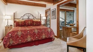 Ein Schlafzimmer mit einem großen Bett, Holzbalken an der Decke, einem Holzstuhl und Blick auf einen Balkon.