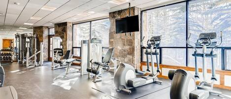 A gym with various exercise equipment, large windows, and a stone accent wall.