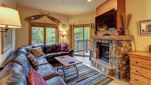 Una sala de estar con chimenea de piedra, sofá de cuero y un televisor de pantalla plana montado encima.