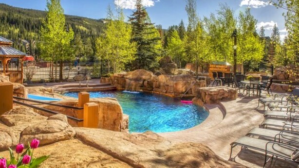 A pool area with a hot tub, surrounded by rocks and trees, and outdoor seating. - 3 Bedroom Condo (Keystone)