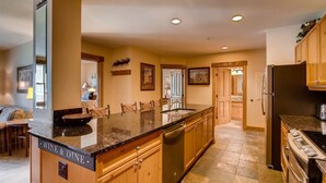 A spacious kitchen with granite countertops, wooden cabinets, a large island, and a built-in dishwasher. - 3 Bedroom Condo (Keystone)