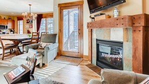A living room with a fireplace, a television mounted above it, and a dining area with a table and chairs. - 2 Bedroom Condo (Keystone)