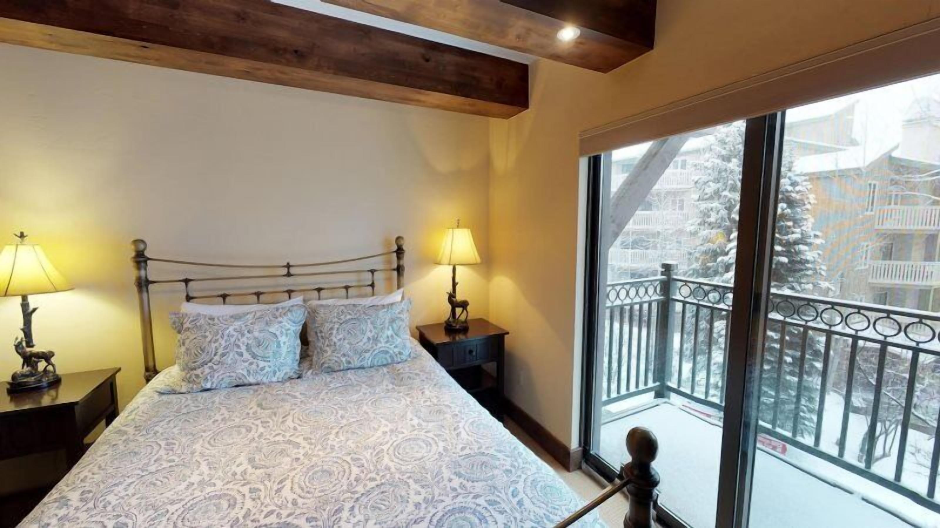 A bedroom with a bed, two bedside tables, and a window with a balcony view.