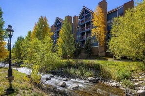 A multi-story building with balconies, surrounded by autumn-colored trees and a stream. - 4 Bedroom Condo (Breckenridge)