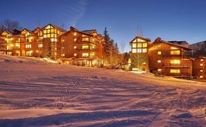A multi-story lodge with large windows and a ski slope in the foreground. - Three Bedroom Condo (Snowmass Village)