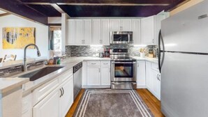 A modern kitchen with white cabinets, stainless steel appliances, and a wooden ceiling. - 3 Bedroom Condo (Keystone)