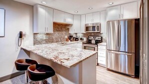 A modern kitchen with white cabinets, a granite countertop, stainless steel appliances, and a built-in island with bar stools. - 4 Bedroom Condo (Breckenridge)