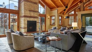 A spacious living area with a fireplace, comfortable seating, and large windows offering a view of the outside. - 3 Bedroom Condo (Vail)