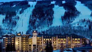 A multi-story hotel with a central tower, surrounded by snow-covered mountains and trees. - 3 Bedroom Condo (Vail)