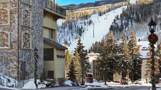 A stone building with a balcony, a ski slope in the background, and snow-covered trees. - 3 Bedroom Condo (Vail)