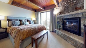 A bedroom with a large bed, a bench, a stone fireplace, and a television. - 3 Bedroom Condo (Vail)