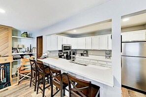 A modern kitchen with white cabinets, stainless steel appliances, and a long island with bar stools. - 3 Bedroom Condo (Keystone)