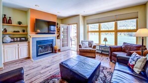 A living room with a fireplace, a television, a sofa, and a view of a lake. - 2 Bedroom Condo (Keystone)