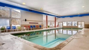 An indoor swimming pool with clear water, surrounded by blue and white chairs, and large windows offering views of the outside. - 2 Bedroom Condo (Keystone)