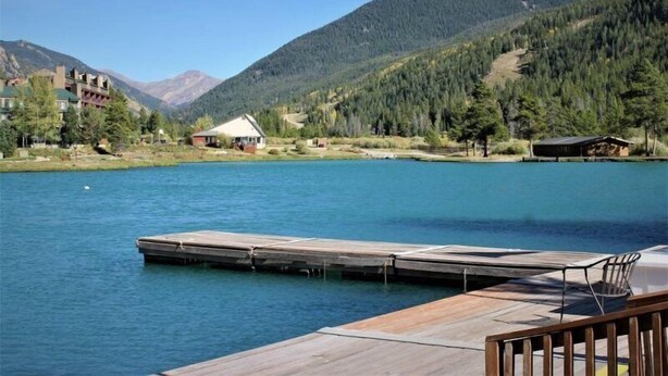 A lakeside view with a wooden dock, a small cabin, and a building with a green roof. - 2 Bedroom Condo (Keystone)