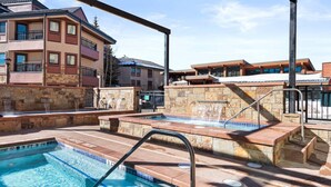 A pool area with a hot tub, stone walls, and a view of buildings. - 1 Bedroom Condo (Breckenridge)
