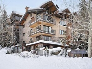 A multi-story building with balconies, a snow-covered entrance, and a sign reading "The Crestwood." - One Bedroom Condo (Snowmass Village)