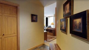 A hallway with wooden doors, framed artwork on the walls, and a desk with a lamp in the background. - 2 Bedroom - Platinium Residence (Vail)