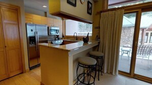 A kitchen with wooden cabinets, a stainless steel refrigerator, a microwave, and a stove. There are two bar stools near the counter. - 2 Bedroom - Platinium Residence (Vail)