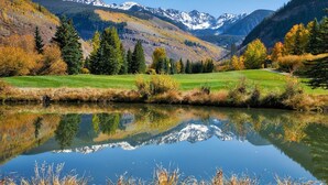 Un lac paisible aux eaux limpides, dont le reflet est parfait, entouré d’un feuillage automnal et dominé par des montagnes en arrière-plan.