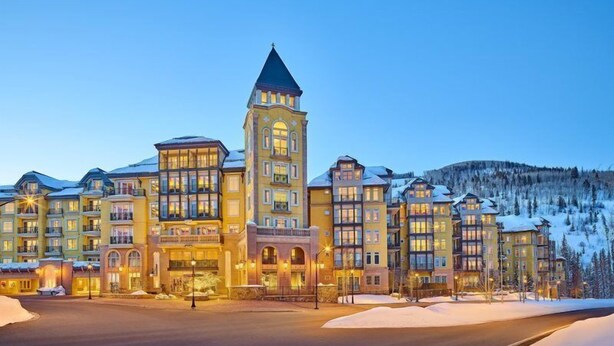 Un grand hôtel à plusieurs étages, doté d’une tour imposante, de toits enneigés et surplombant un paysage montagneux.