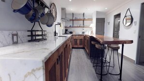 A modern kitchen with a marble countertop, wooden cabinets, and a bar area with stools.