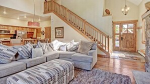 Ein geräumiges Wohnzimmer mit einem großen grauen Ecksofa, einer Holztreppe und einer Küche im Hintergrund.
