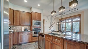 Uma cozinha moderna com armários de madeira, eletrodomésticos de aço inoxidável, bancada de granito e iluminação pendente.