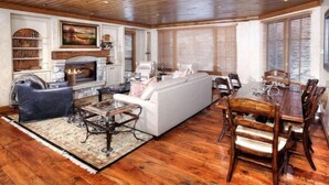 A spacious living room with a fireplace, white sofa, dining table, and wooden flooring. - 3 Bedroom - Elkhorn Lodge (Avon)