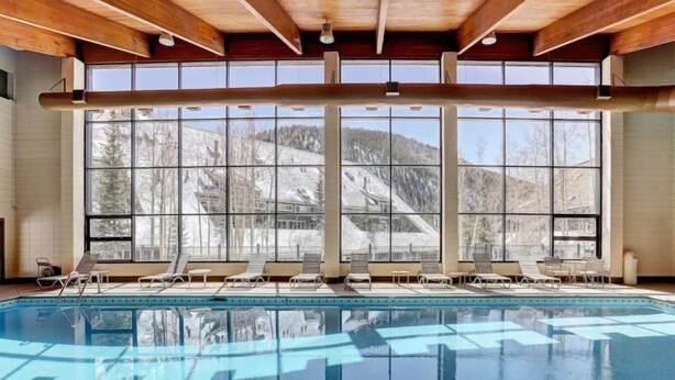 Una amplia piscina cubierta con vistas despejadas a un paisaje montañoso nevado a través de grandes ventanales.